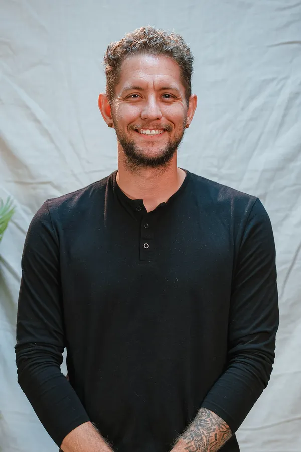 Joshua Shaw smiling in a black henley, against a white backdrop.