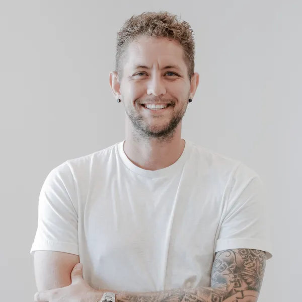 Joshua Shaw smiling, in a white tee with his arms folded, against a light background.