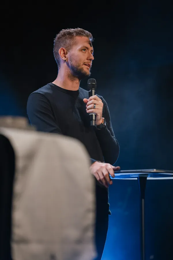 Joshua Shaw teaching with a microphone beside a lectern, in a dark room.